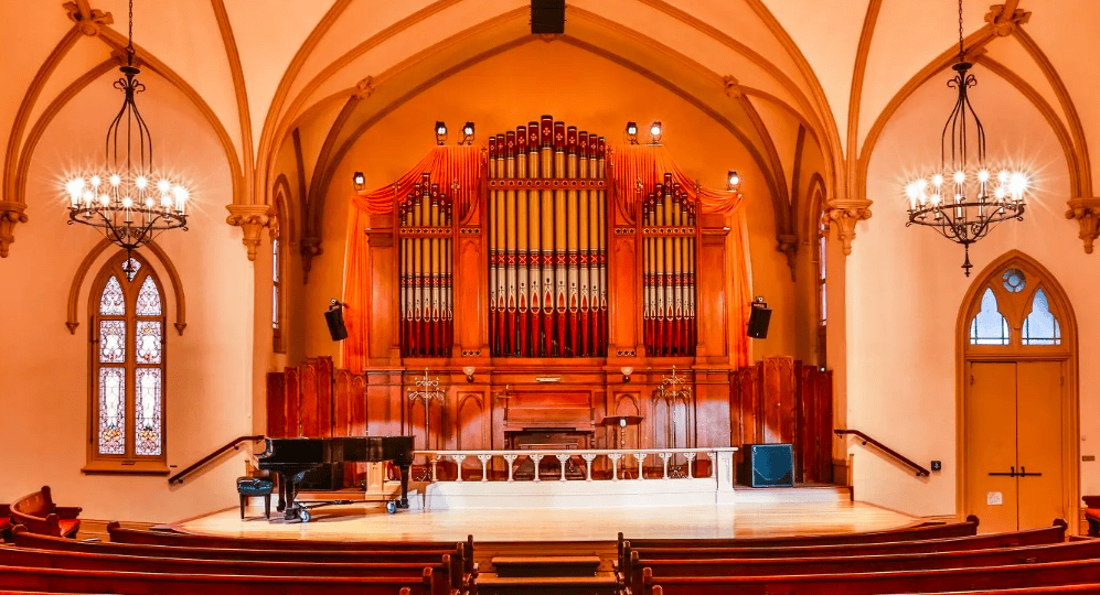 photo old church interior. There's a piano on the stage and a large organize behind it.